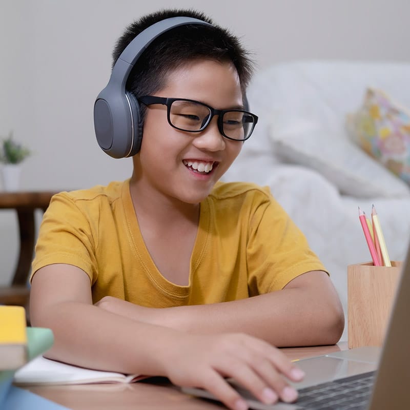 Asian student wearing headphones and working on the computer.
